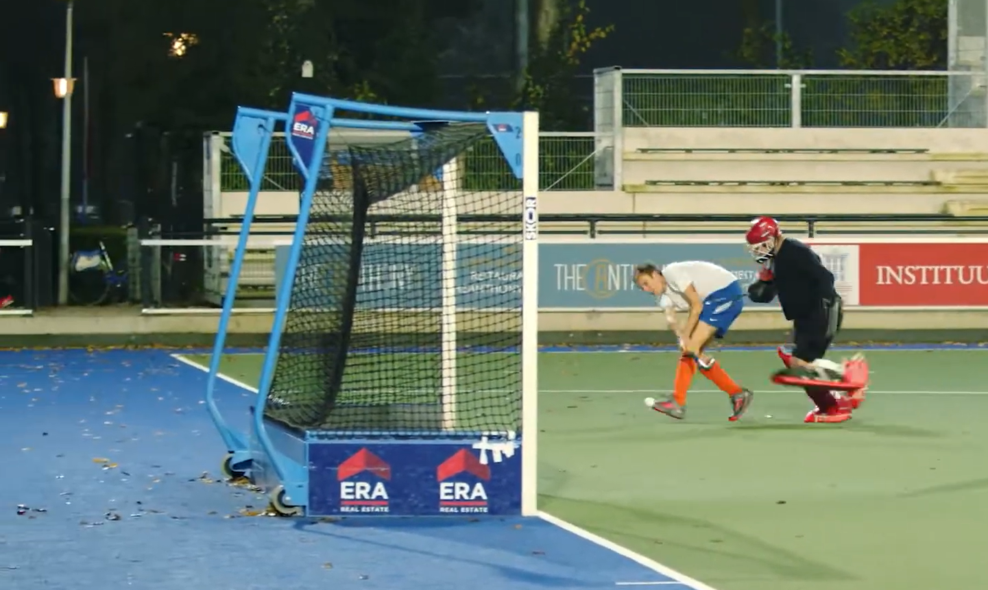 Fast-paced field hockey game with goalies, players, and a goalpost on an outdoor sports court, highlighting athletic performance and team sports.