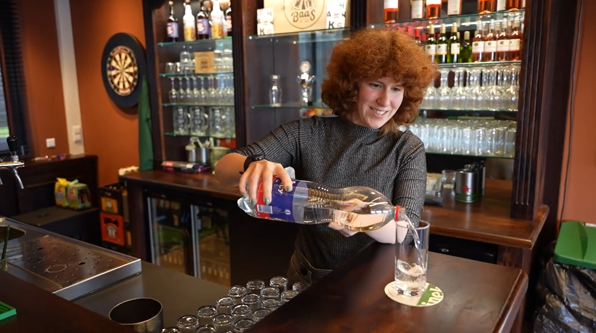 Refreshing water being poured into a glass at a cozy bar or cafe, with shelves of bottles and glasses in the background, highlighting a friendly hospitality environment and career opportunities in hospitality.