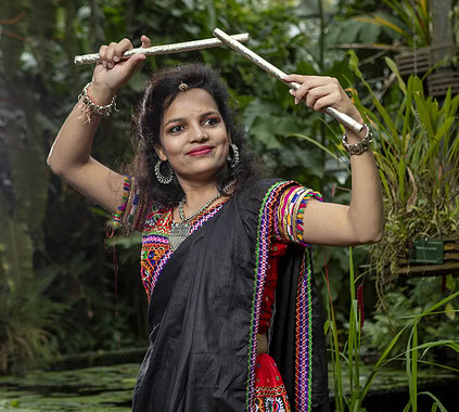 A woman in traditional Indian attire holding a gardening tool in a lush green botanical garden.