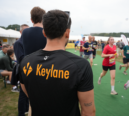 Diversity of people participating in a running event, with a focus on a person wearing a Keylane-branded shirt, emphasizing careers, professional growth, and active workplace culture at Keylane.